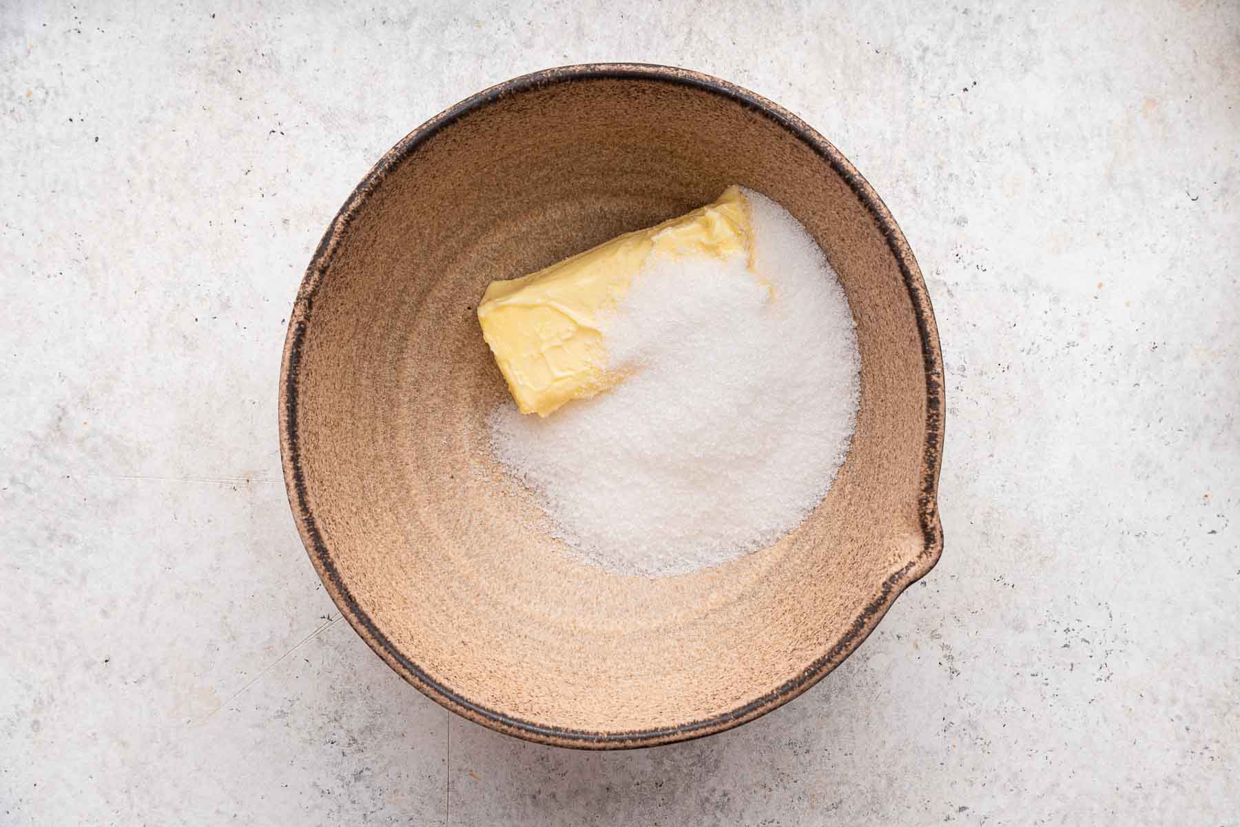 A stick of butter with granulated sugar in a brown bowl.