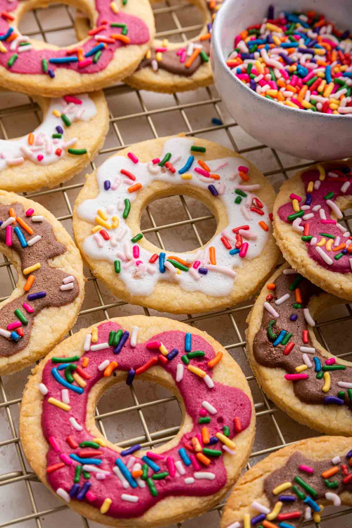 Donut cookies with pink, white and brown frosting and sprinkles on a wire rack.
