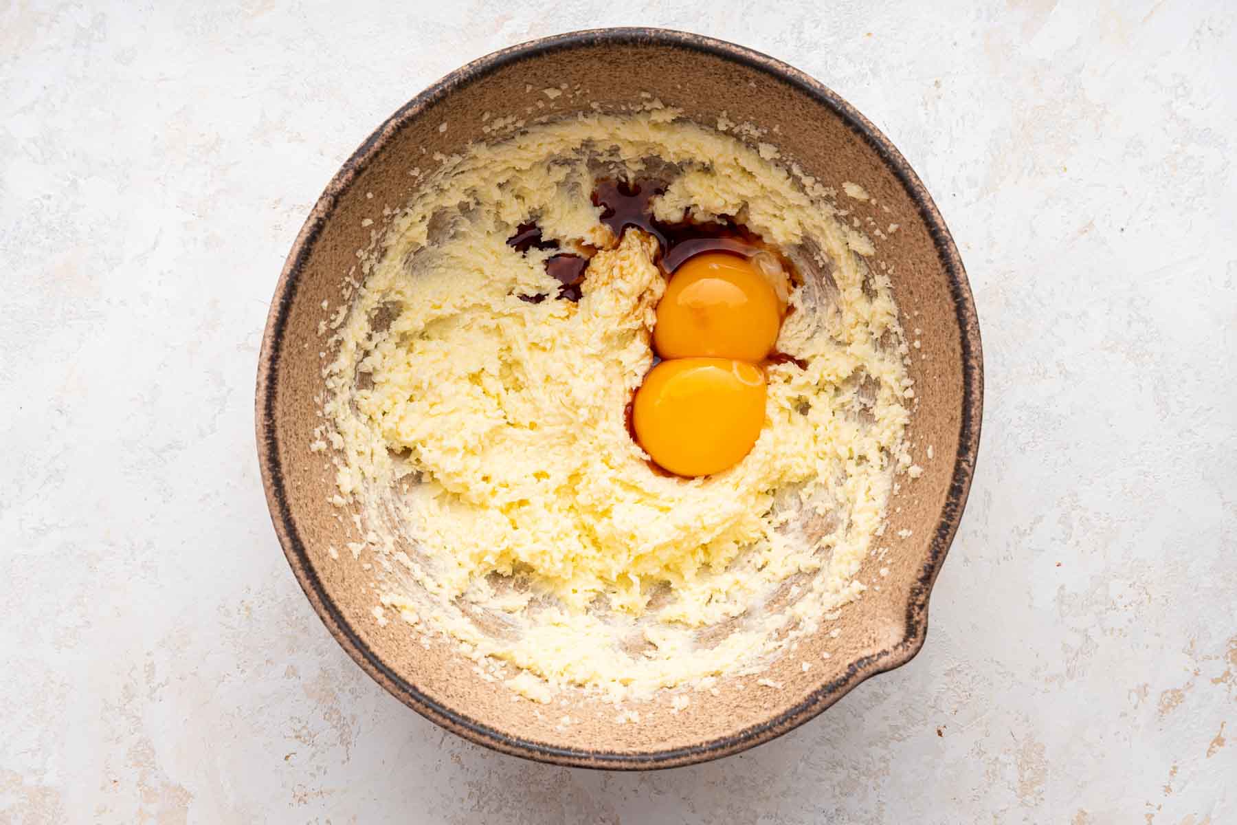 Egg yolks and vanilla over cookie dough in brown bowl.