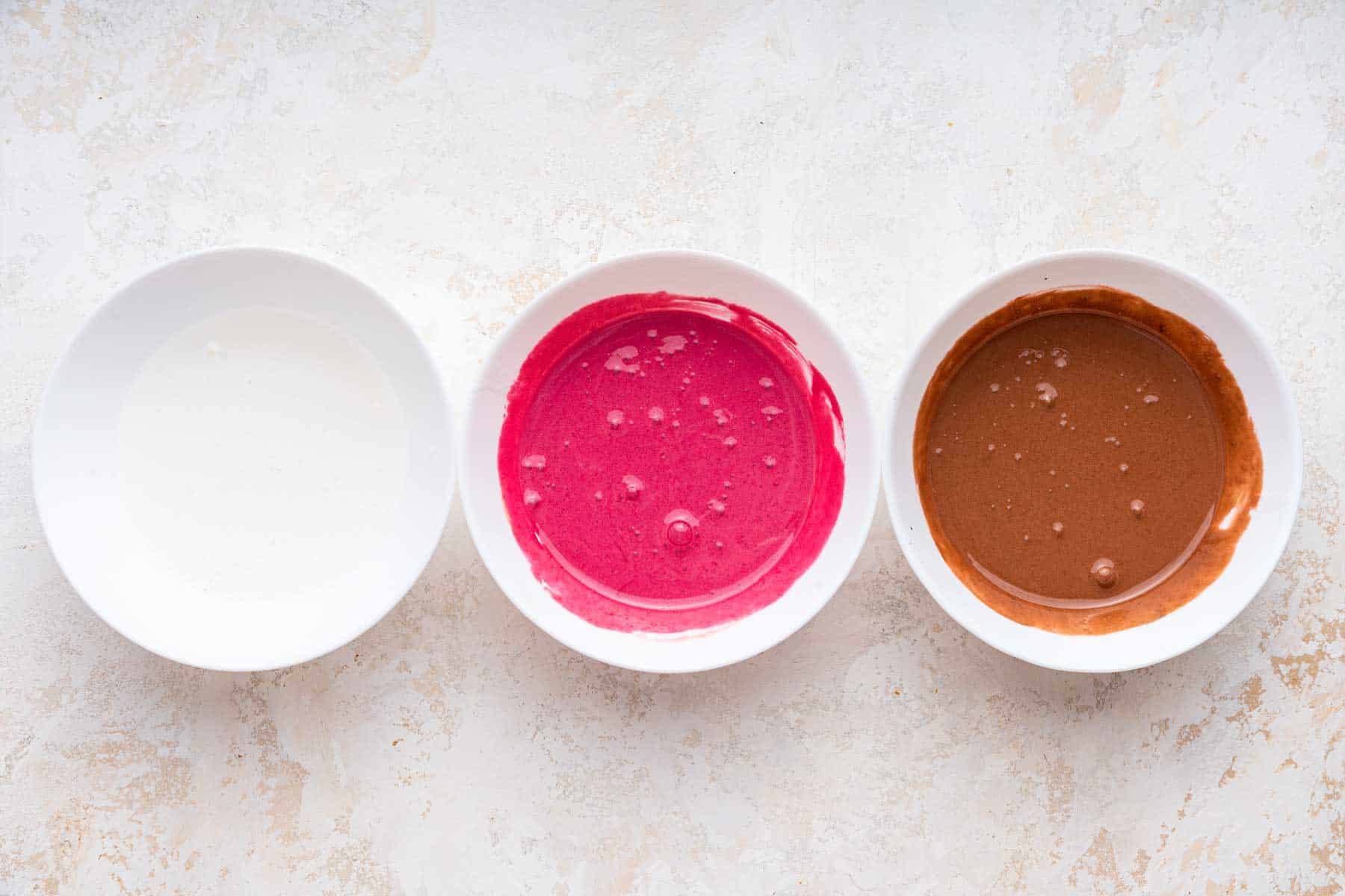 Three bowls of white, pink, and brown frosting for cookies.