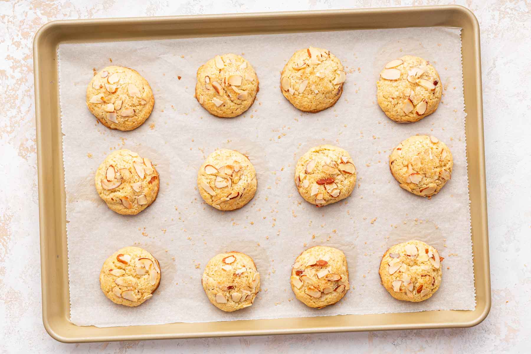 One dozen almond croissant cookies baked on a gold baking sheet.