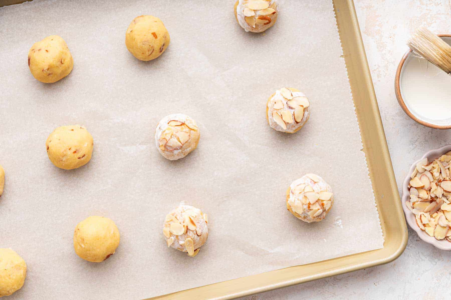 Yellow cookie dough balls brushed with cream and sprinkled with sliced almonds.