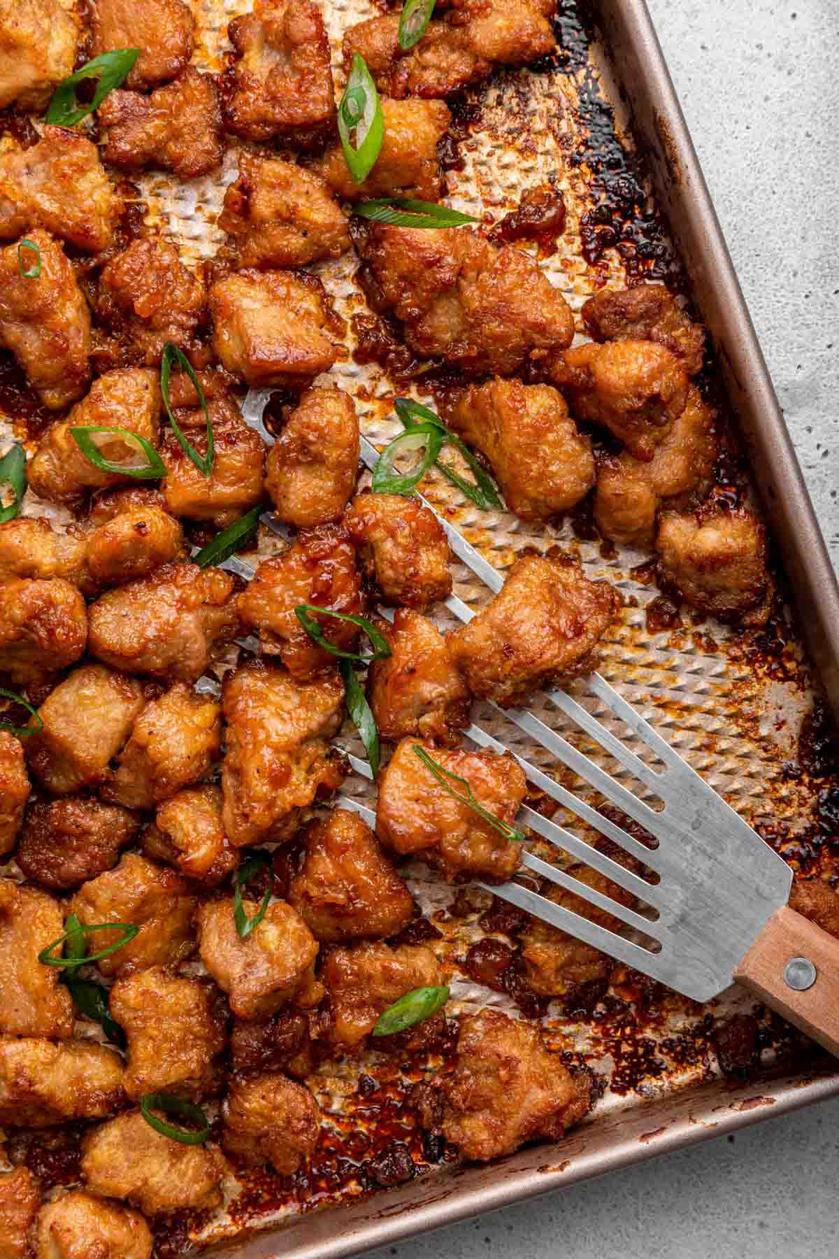Honey garlic pork pieces on baking sheet with spatula sprinkled with scallions.
