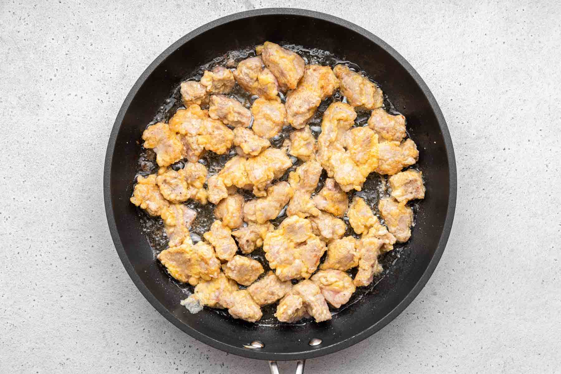 Light brown crusted pieces of meat in a black frying pan.