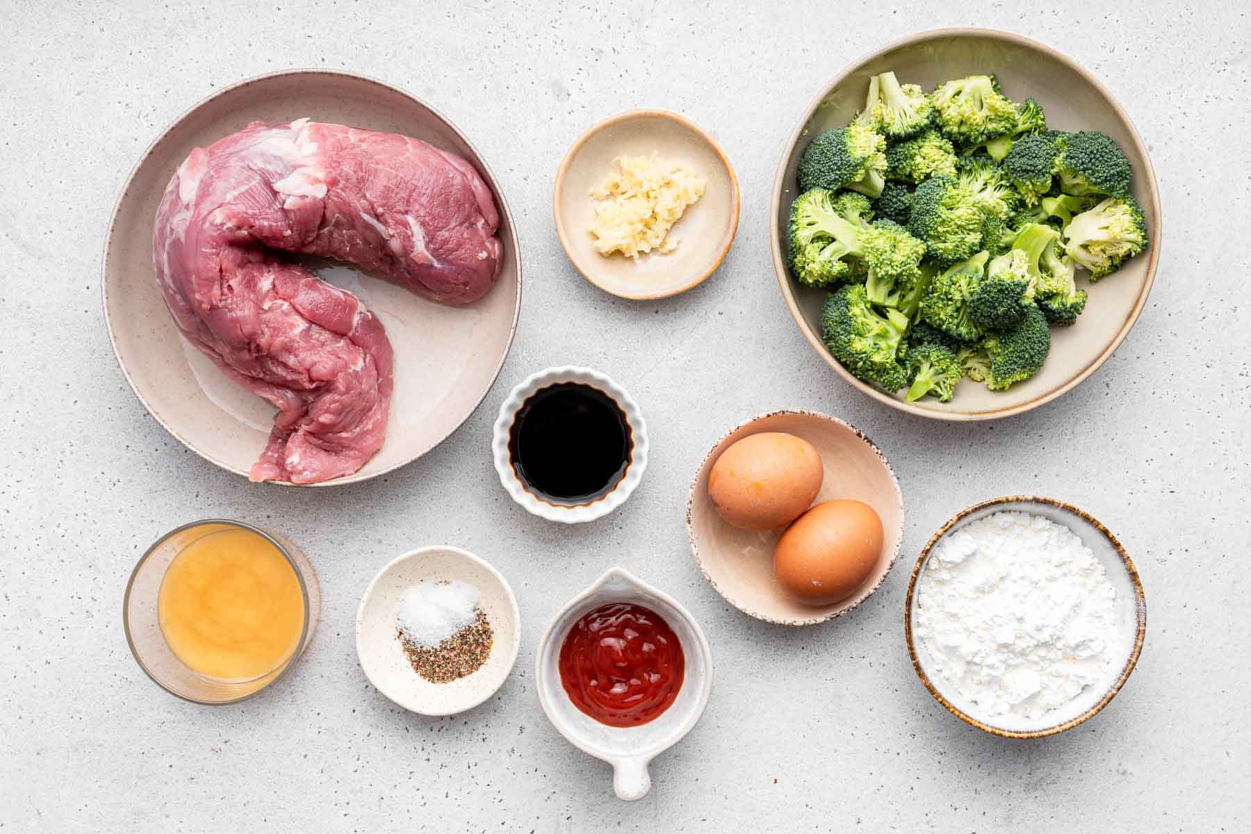Small bowls of broccoli, egg, cornstarch, and pork tenderloin on light grey counter.
