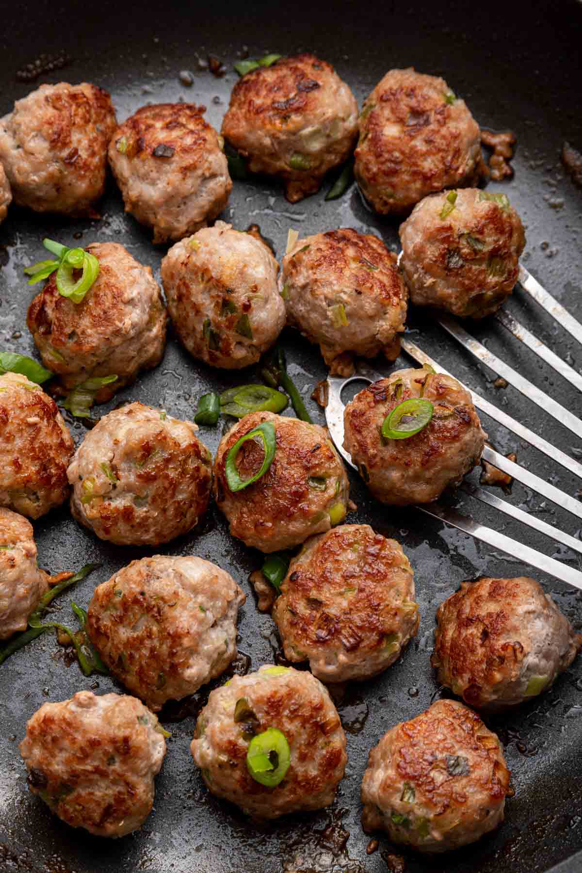 Perfectly round pork meatballs in a black cast iron skillet.