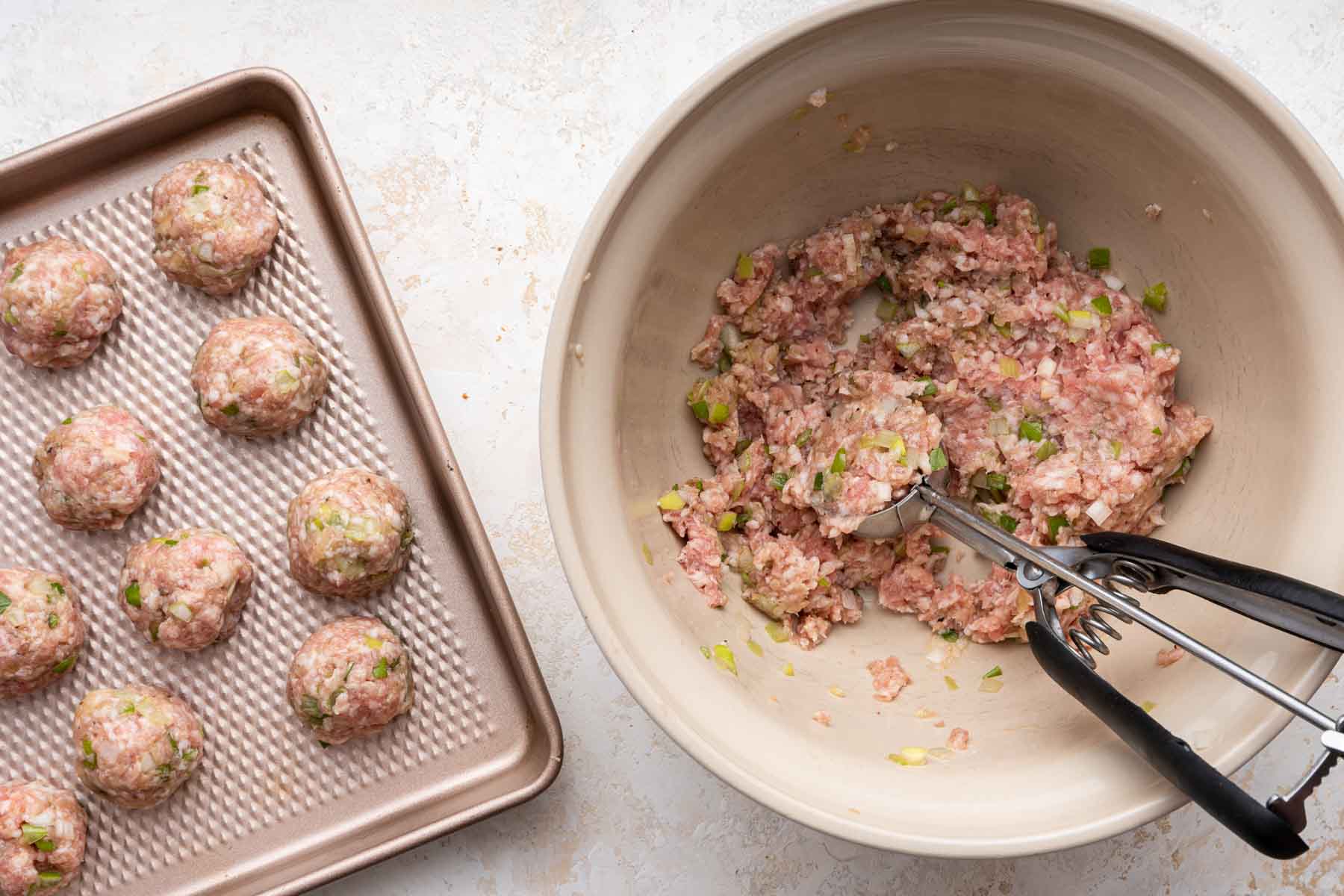 Using a cookie scoop to make pork meatballs and placing them on a cookie sheet.