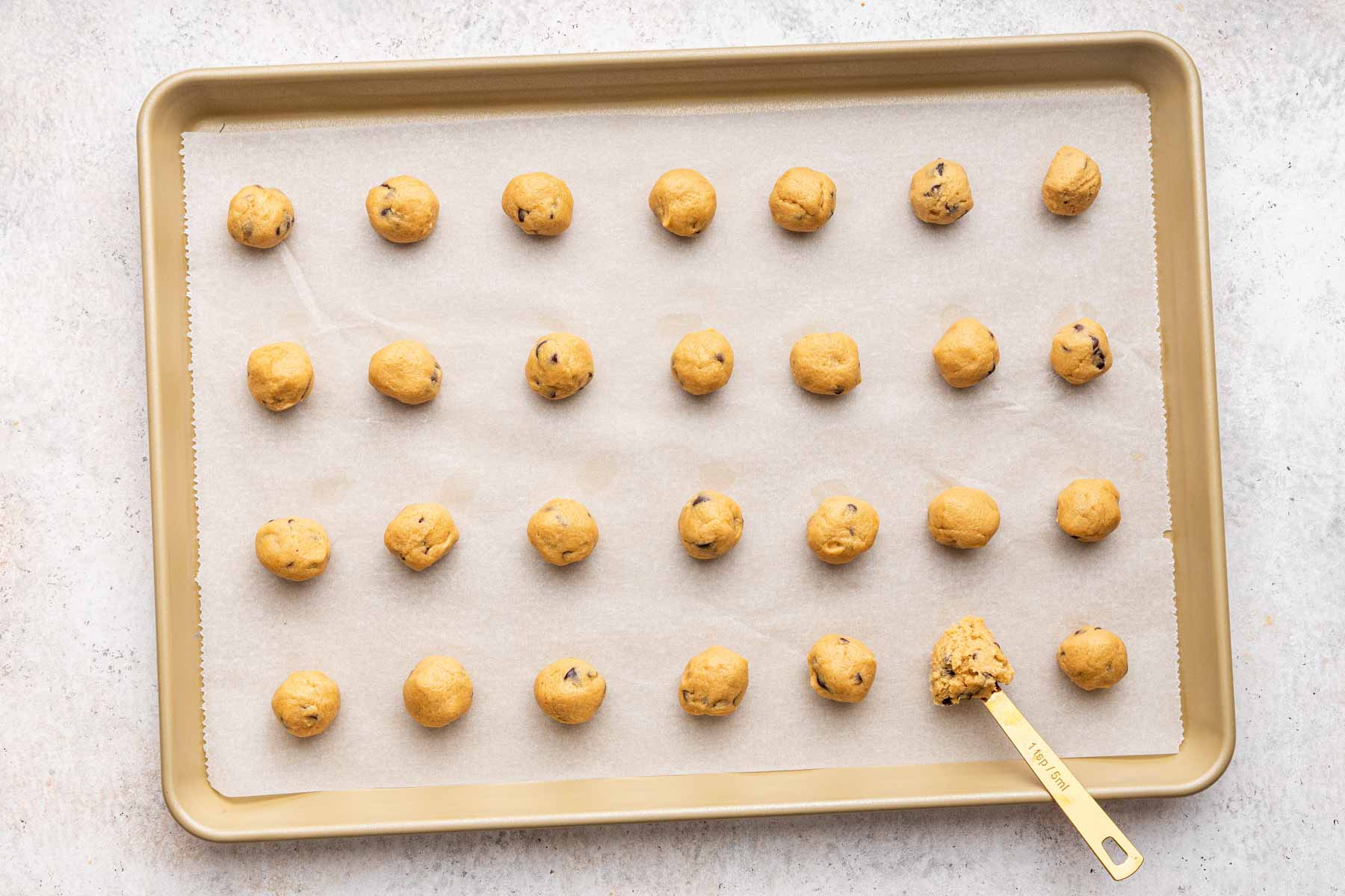 Forty mini chocolate chip cookies on a baking sheet with a teaspoon.