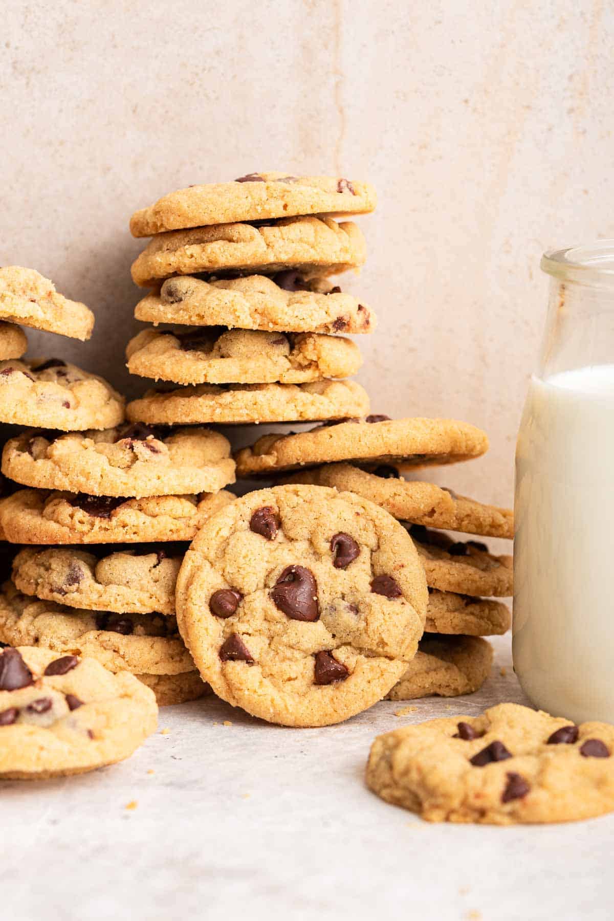 Stack of mini chocolate chip cookies against wall with milk on side.