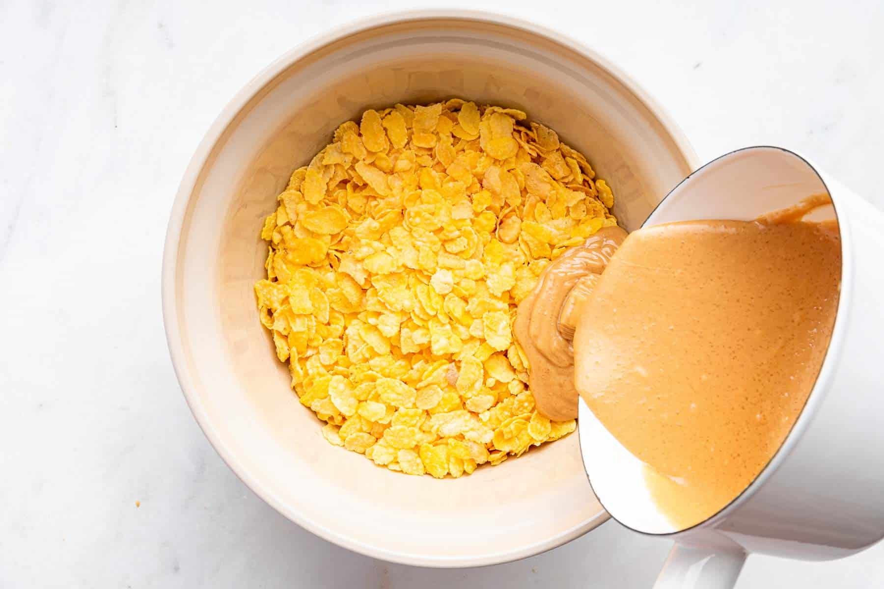 Melted peanut butter being poured over a bowl of cornflakes.