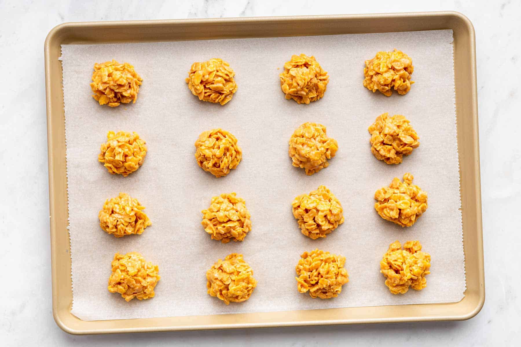 Sheet pan with 16 cornflake cookies cooling on it.