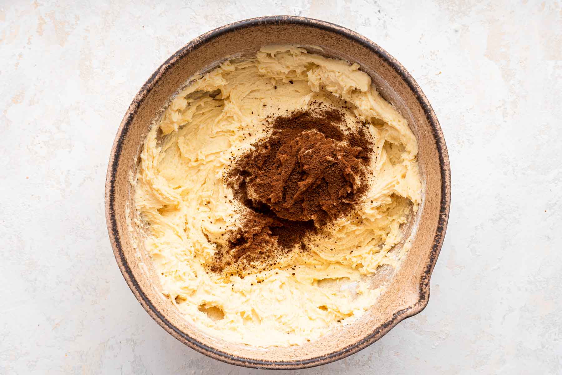 Yellow dough in brown bowl with espresso powder on top.